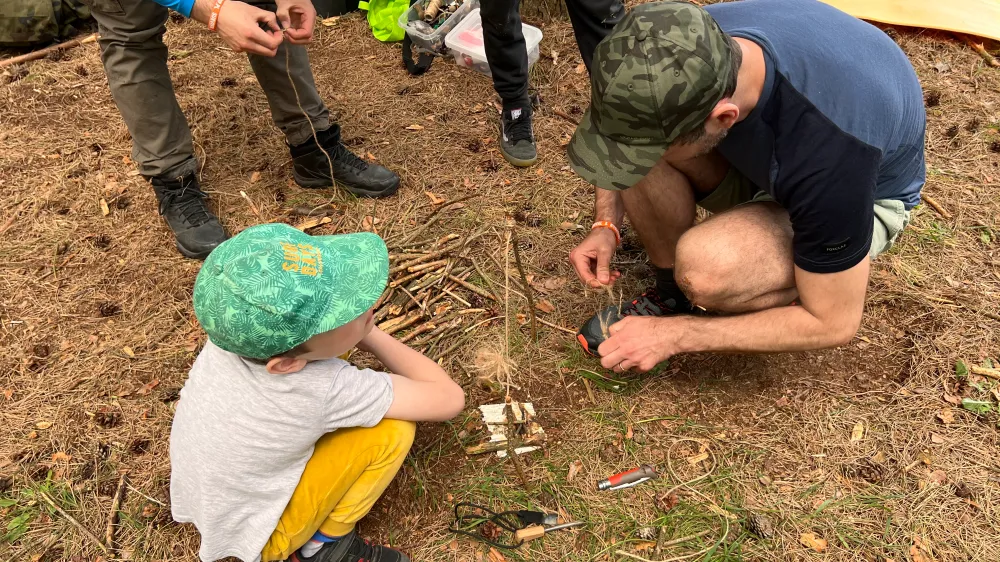 Tata z dzieckiem na survivalu. Dziecko uczy się od ojca jak rozpalić bezpiecznie ogień.